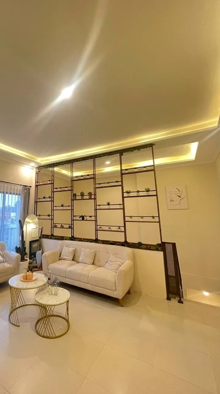 Ruang tunggu dengan sofa krem, rak tanaman, dan meja marmer bulat