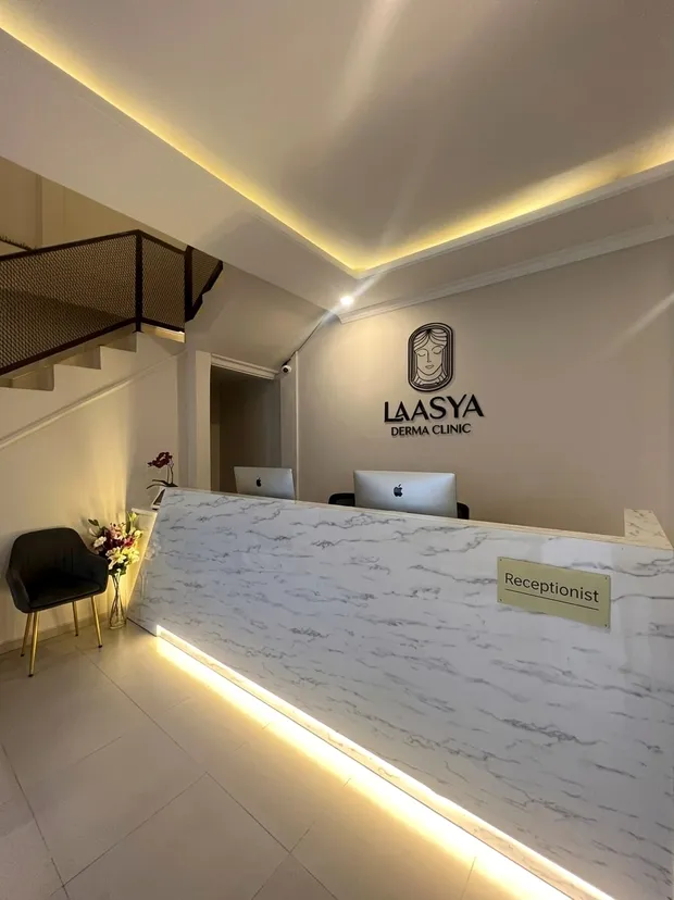 Meja resepsionis marmer Laasya Derma Clinic dengan logo timbul di dinding